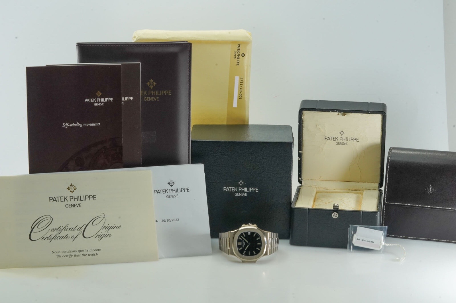 White gold sports watch with a black dial shown with its full set of boxes, certificate and papers